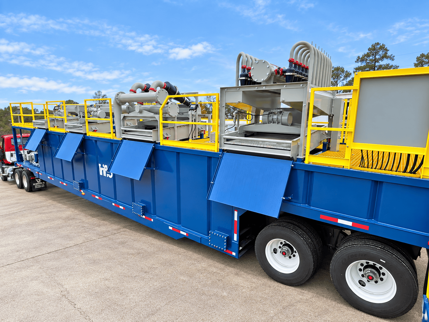 Triflo ES-1000R environmental dewatering system with blue tank, yellow safety railings, shakers, hydrocyclones, and piping mounted on a trailer.