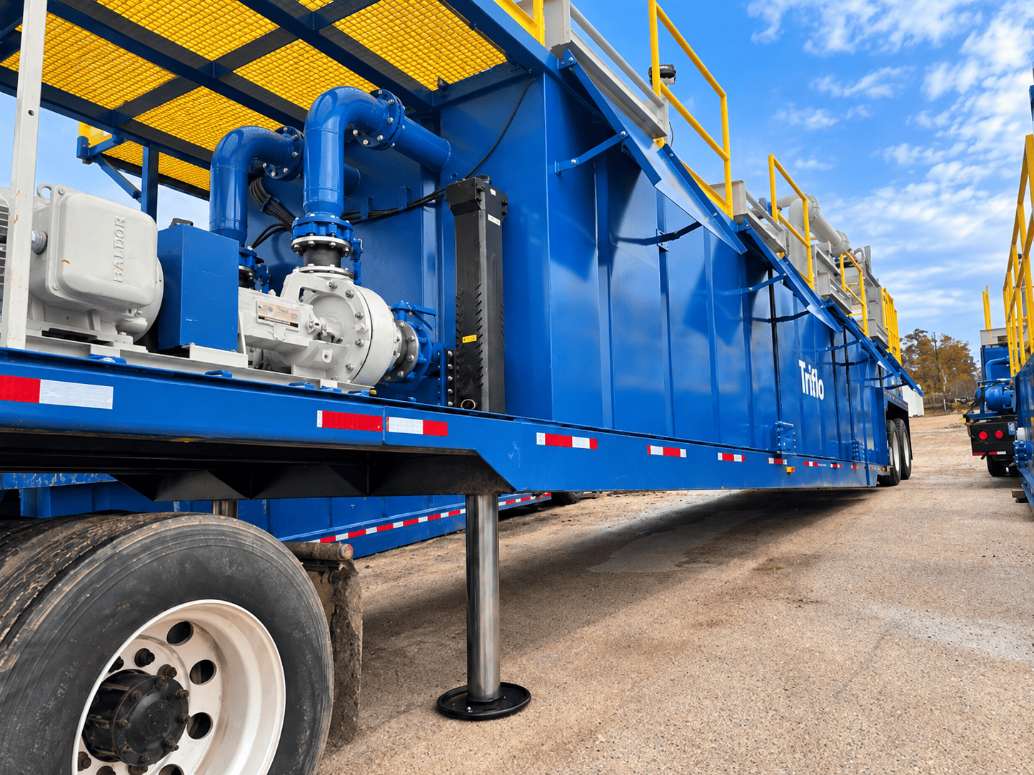 Low-angle view of a Triflo ES 1000R environmental dewatering system featuring pump and piping assemblies, yellow grated walkways and safety rails, and a stabilizing jack.